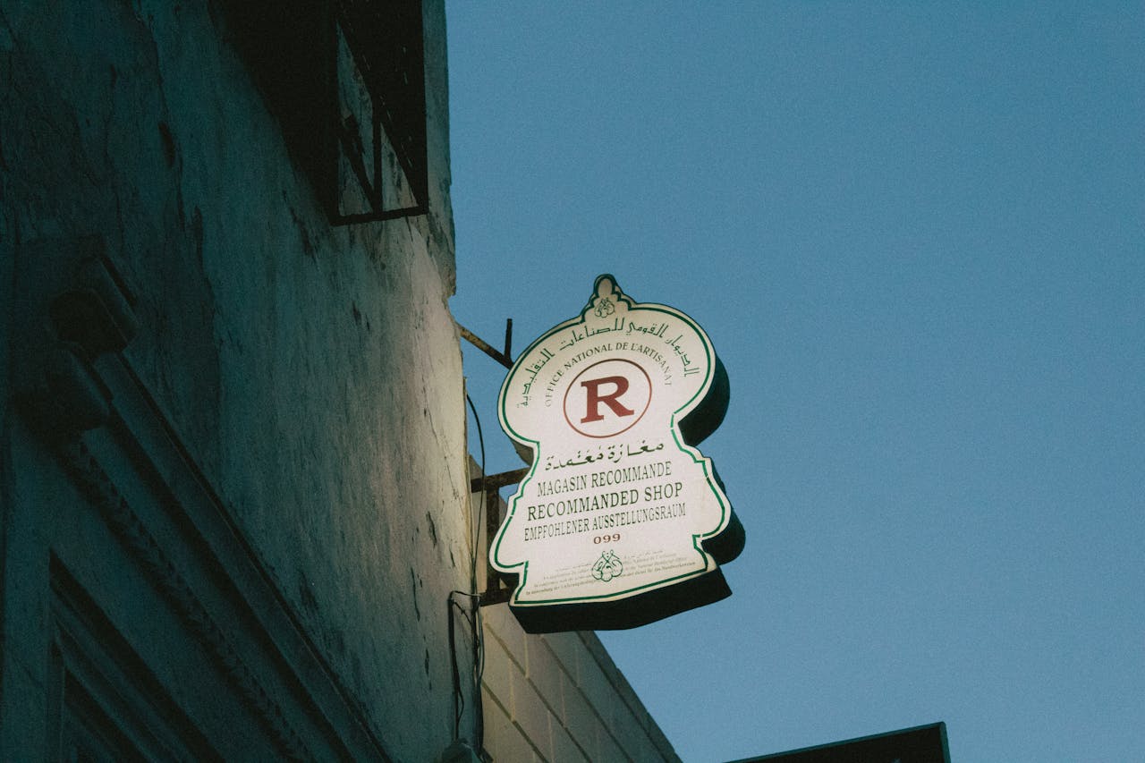 Mastering the First Impression: Your intriguing post title goes here A glowing shop sign with Arabic, Latin, and German script lights up an urban street corner at dusk.